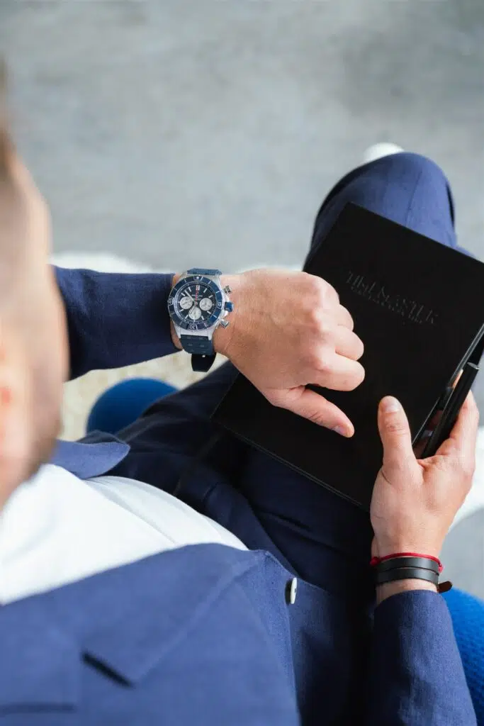 Pohľad na človeka z hora, ktorý sa pozerá na hodinky a drží v ruke zápisník TIMEMASTER.